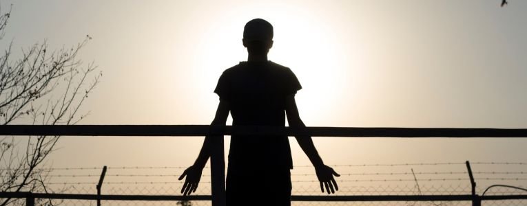 Silhouette of Man Standing Near Fence during Sunset