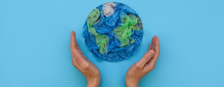 Hands Holding Planet Earth Made from Plastic Disposable Packages on Blue Background. save the World, Creative, Environment Pollution or World Earth Day Concept. Top View