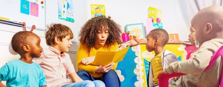 Teacher Reads a Book to Group of Kids in Nursery